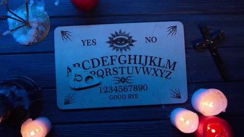 Close Up Video of a Wooden Ouija Board on a Table Surrounded By Candles and a Cross in Flashing