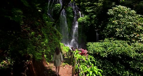 Female explorer walk towards scenic jungle waterfall Banyu Wana Amertha. Aerial