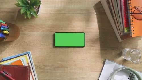 Top down view of a mock up green screen smartphone on a wooden office desk