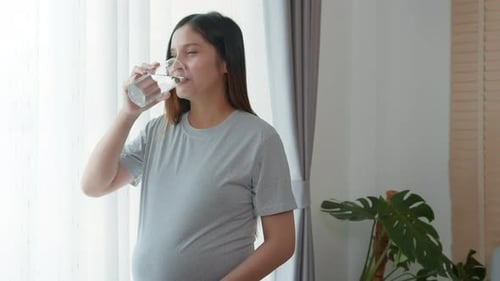 Young pregnant woman drinking water at home