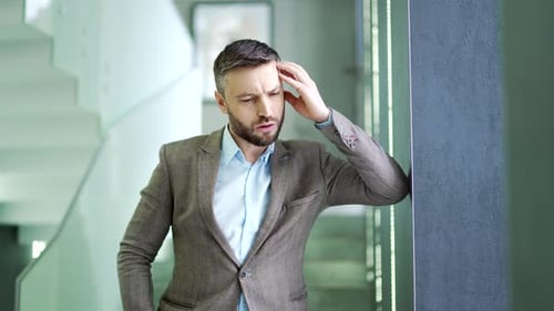 Overworked businessman suffering from headache standing in corridor or hall of modern business