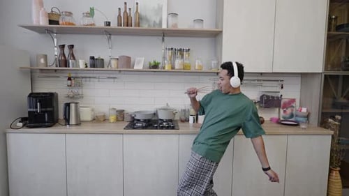 Jeune homme africain au casque chantant dans un fouet comme un microphone dans la cuisine