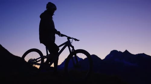 A mountain biker is standing on top of a ridge during sunrise