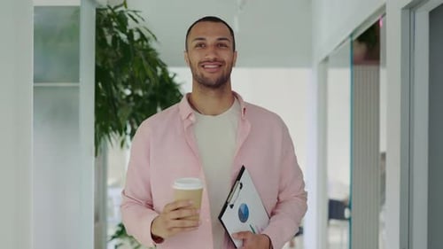 Smiling Man Walking with Coffee and Charts in Office