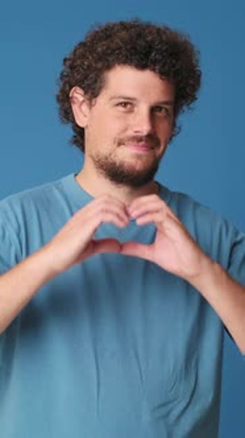 Man showing representing heart in the shape of fingers gesture isolated on blue background studio