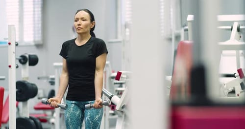 A Fit Middle Aged Woman Training Biceps with Dumbbells During an Intense Gym Workout