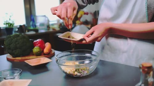 Person adds spice to vegetable salad indoors