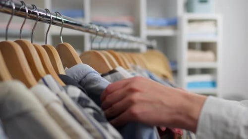 Person choosing shirts from hanging closet rack