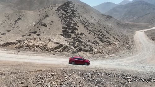 Imagen panorámica aérea de un viaje por carretera con un automóvil rojo en una carretera rural seca y polvorienta con piedras a lo largo del