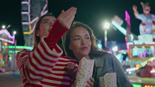 Two Friends Enjoy Popcorn at Amusement Park at Night