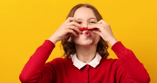 Une écolière drôle fait une moustache sur son visage avec un crayon rouge