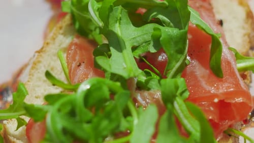 Blick von oben auf frisch geschnittenes Brot mit geräuchertem Lachs und Rucolasalat.