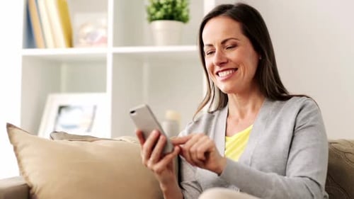 Happy Woman Using Smartphone on Sofa at Home