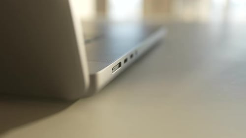 Extreme Nahaufnahme eines nicht erkennbaren Mannes, der ein magnetisches USB-C-Netzkabel in einen modernen Laptop auf dem Schreibtisch steckt