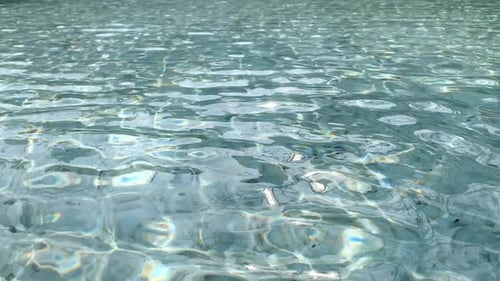 Surface rippling in a swimming pool with clear refreshing water - background texture