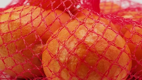 A group of tropical tangerine fruits in a mesh package rotate on a white background.