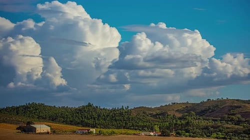 Blue cloud with big white clouds moving in a timelapse, over a meadow with trees and hills.