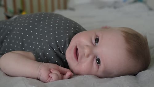 Smiling Infant Laying on a Grey Blanket