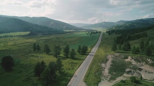 Aerial View of an Asphalt Road in Rural Area Between Green Fields and Hills