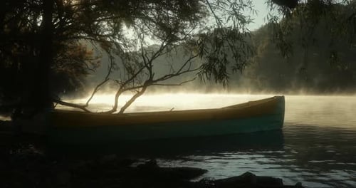 Un bateau flottant au lever du soleil sur un magnifique lac. Les rayons du soleil se reflètent sur l'eau et les arbres.
U