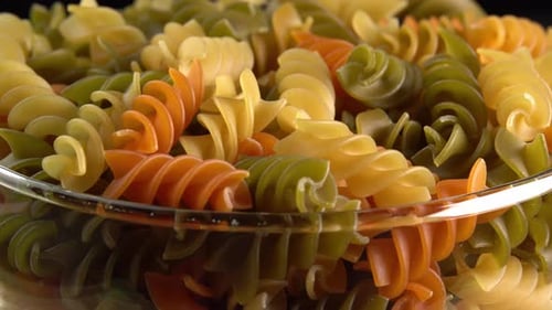 Multicolored italian pasta Fusilli or Rotini rotating in glass bowl side view. Durum wheat pasta