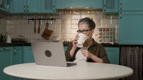 Woman Video Conferencing in Kitchen Drinking Coffee
