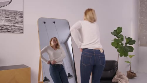 Unhappy Overweight Mature Woman Trying to Fit Into Small Jeans at Home
