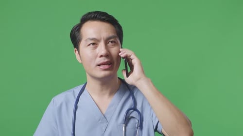 Close Up Of Asian Male Doctor With Stethoscope Talking On Smartphone While Standing On Green Screen