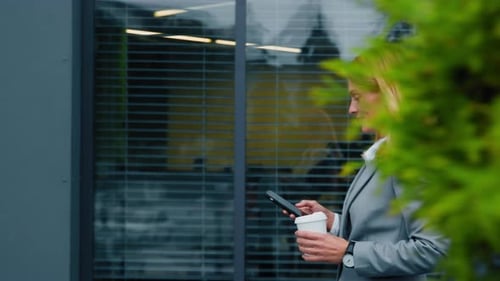 Smiling Businesswoman in Suit Walking Street Holding Paper Cup with Coffee Communicating Via Email