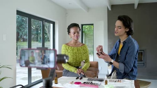 Maquilladora y mujer afroamericana en el escritorio sosteniendo el rubor de forma compacta y barriendo las mejillas para el tutorial