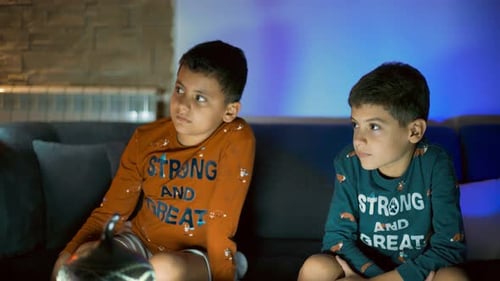 Two Young Boys Sitting on a Couch at Night