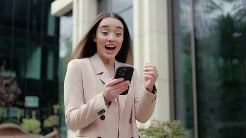 Excited Woman Celebrates Success on Smartphone in City