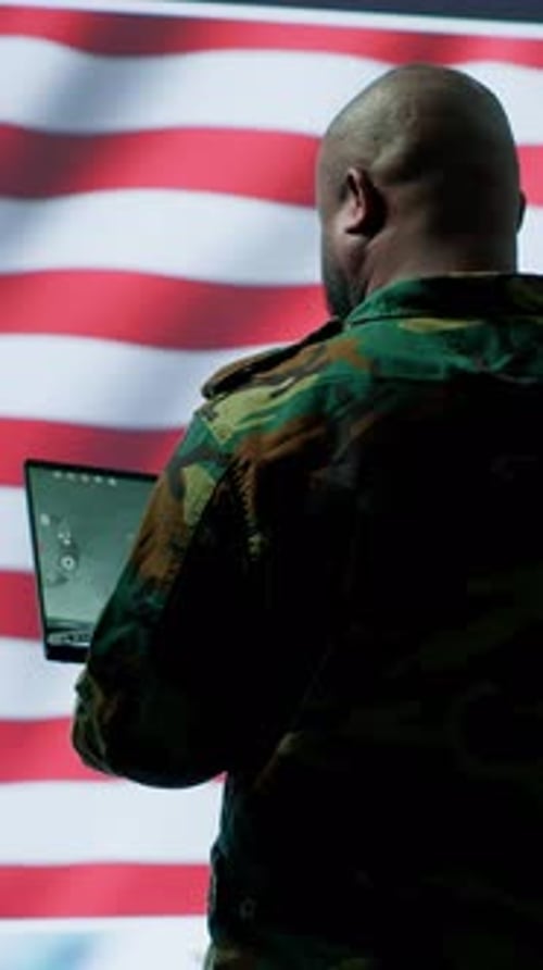 Adult in Camouflage Using Laptop by American Flag