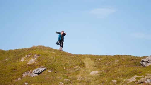 Adult Walking with Camera Equipment on Hilltop