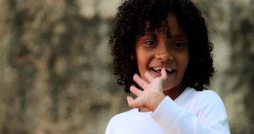 Brazilian little girl waving hello to camera. child waves hi