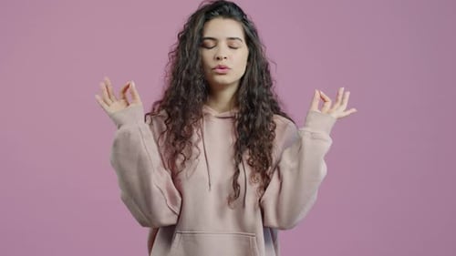 Câmera lenta de garota estressada meditando em pé sozinha sobre fundo rosa