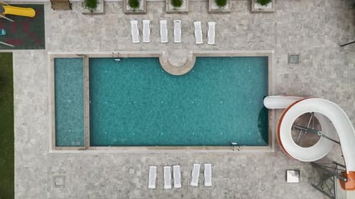 Aerial Video of Outdoor Pool with Aqua Slide and Empty Loungers in Resort Courtyard