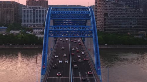 Aerial View of a Blue Bridge with Cars Crossing Over a River at Sunset with a City Skyline in the