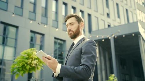 stylish bearded businessman in formal business suit standing working with tablet in hands