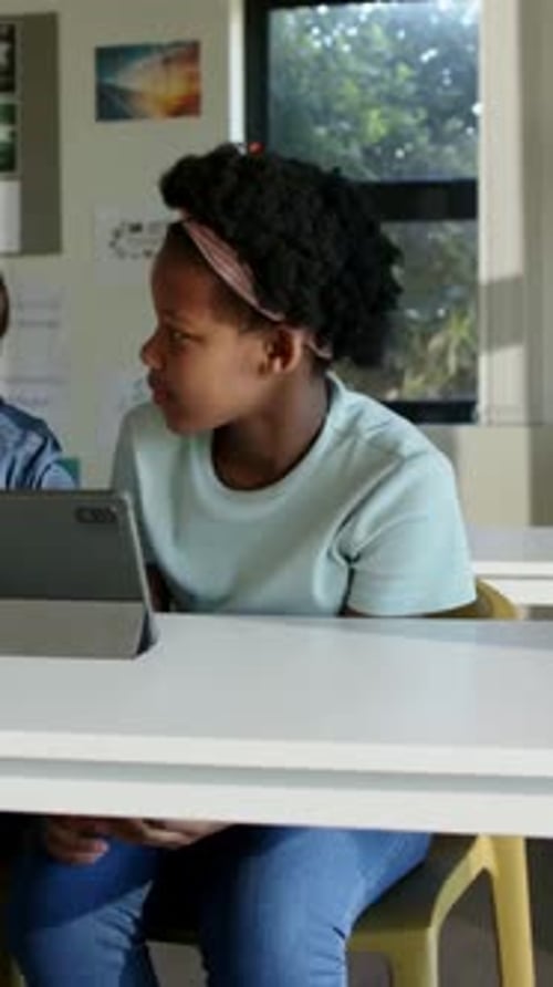 Vertical video: Reading female student in teal shirt turning to peer speaking in class with tablet