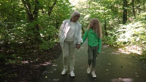 Front View Beautiful Senior Woman and Cute Teenage Girl Talking Walking in Slow Motion Holding Hands