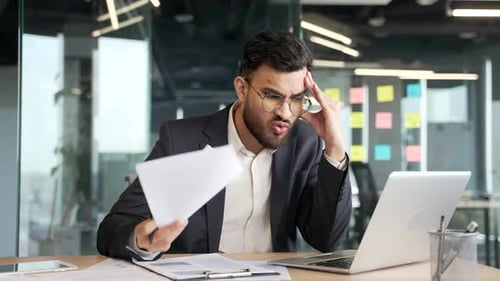 Stressed Man Reviews Documents at Office Desk