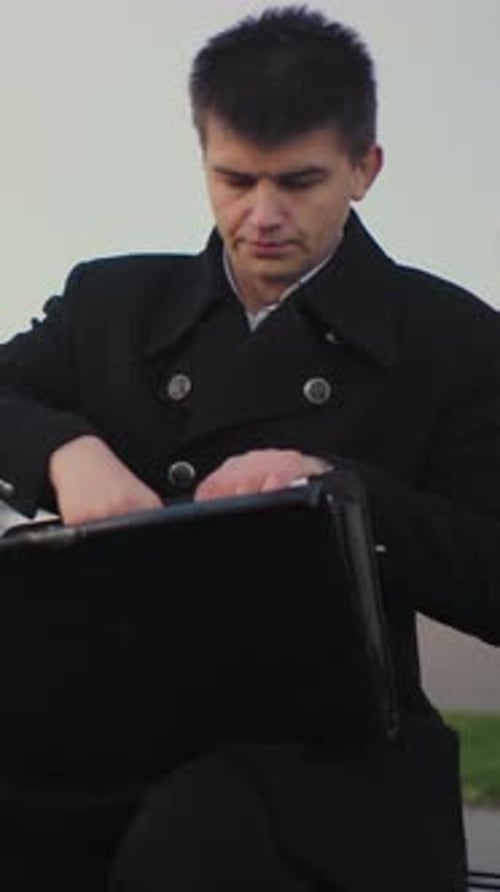 Young man in overcoat opens briefcase outside