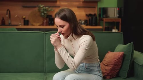 Worried Sad Brunette Woman Reflects While Sitting on a Green Sofa in the Living Room at Home