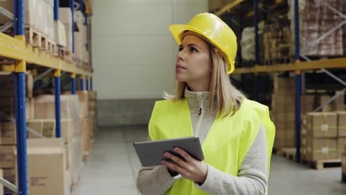 Young woman warehouse worker inspecting stock with tablet computer
