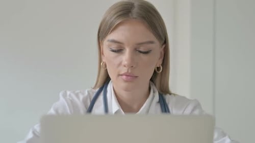 Close up of Female Doctor Smiling at Camera while Working on Laptop in Clinic