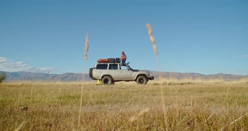 Woman Stands on SUV in Remote Field