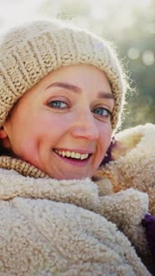 Une femme en pull confortable et chapeau sourit chaleureusement à l'extérieur pendant une journée ensoleillée