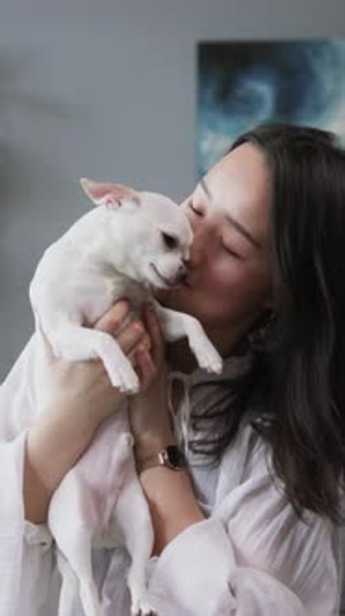 Smiling Woman Holding and Kissing Small White Dog