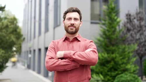 Portrait of confident bearded businessman standing outside office building with arms crossed. Man